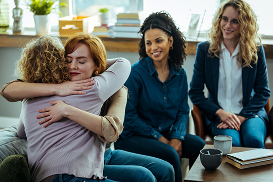 Two women hug each other as others look on.