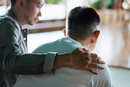 A man supportively resting his hand on another's shoulder
