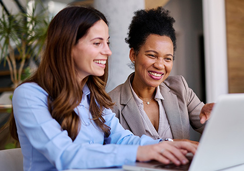 Two businesswomen chat while looking at a laptop.