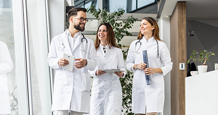 Three doctors stand together proudly in the hallway of a brightly lit hospital.