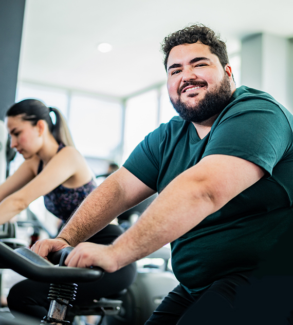 An image of a man excercising on a cycle machine in a gym with a smile on his face.