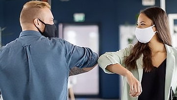 Two people bump elbows while wearing masks