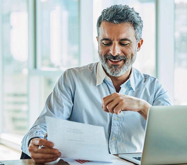 Man sitting at desk reading paperwork at computer