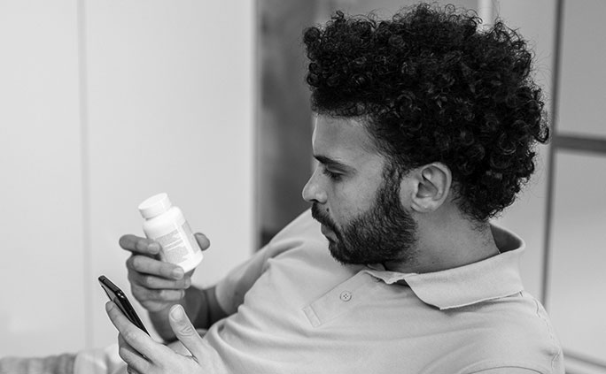 A man holds his mobile device and a prescription bottle