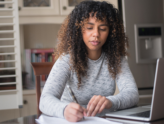 Woman sitting at a laptoptaking notes on paper