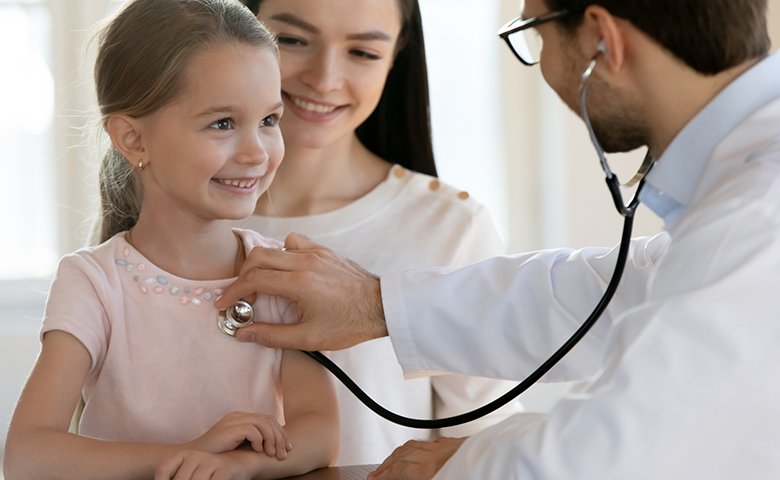 A little girl smiles as a doctor checks her heart rate. 