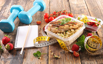 A measuring tape, a pair of weights and a notebook sit on a table. 