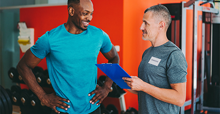 A amn in a gym speaking with his personal trainer