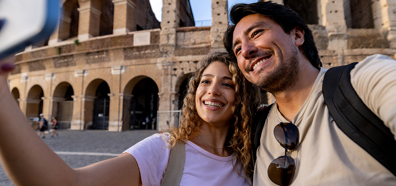 Two tourists smile while taking a photo in front of the Coliseum.