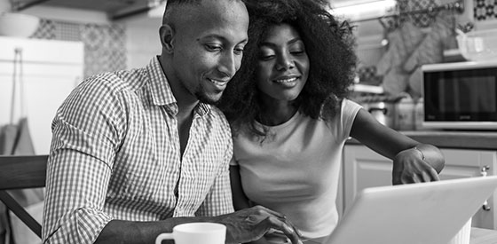 A couple sitting at a kitchen table looking at a laptop