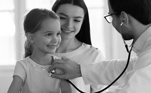 A little girl smiles as a doctor checks her heart rate. 