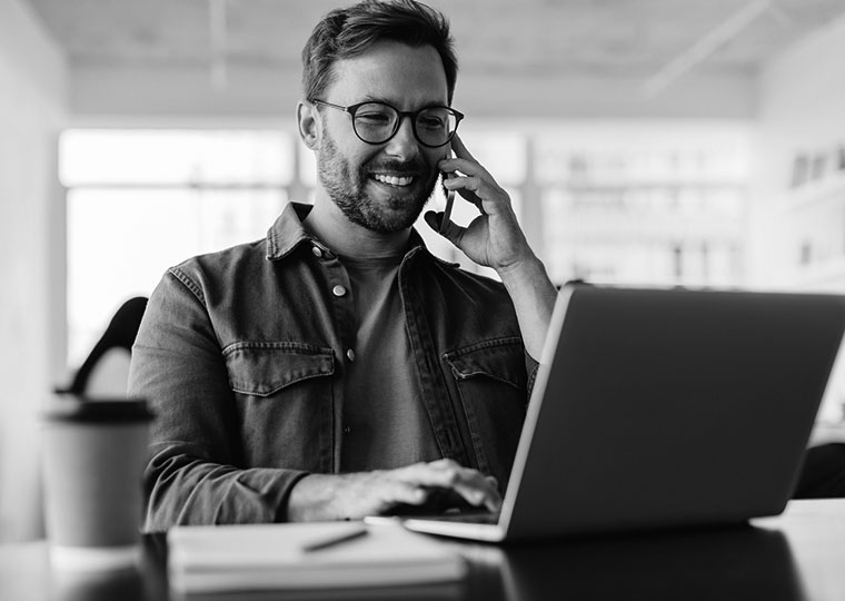 A man on his phone looks at a laptop