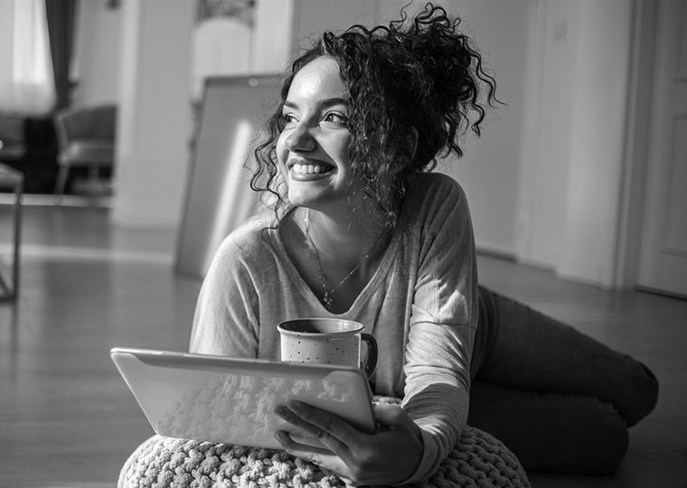 A woman drinks coffee and looks up from her tablet.