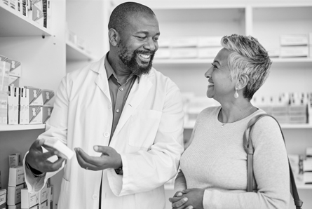  A pharmacist and woman smile while talking about a medication