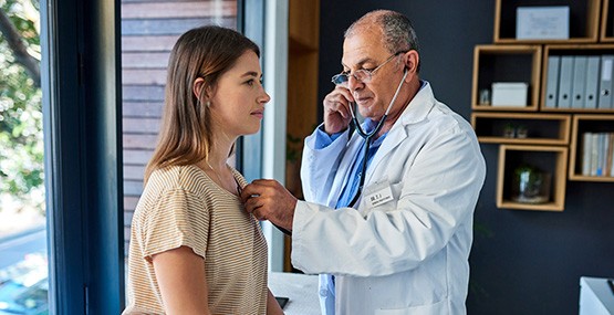 A male doctor with a stethoscope listens to a female patient‘s heart during a checkup.