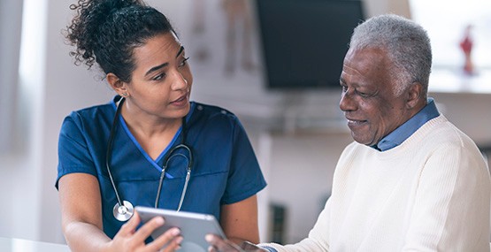 A female doctor and older male patient look at a tablet.
